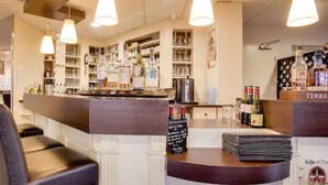 A bar area with shelves stocked with bottles and glasses, a counter with a menu, and hanging pendant lights. - Brit Hotel La Cote Des Havres (Lessay)