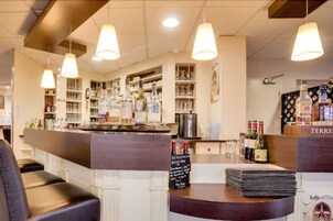 Una zona de bar con estanterías llenas de botellas y copas, una barra con un menú y lámparas colgantes.