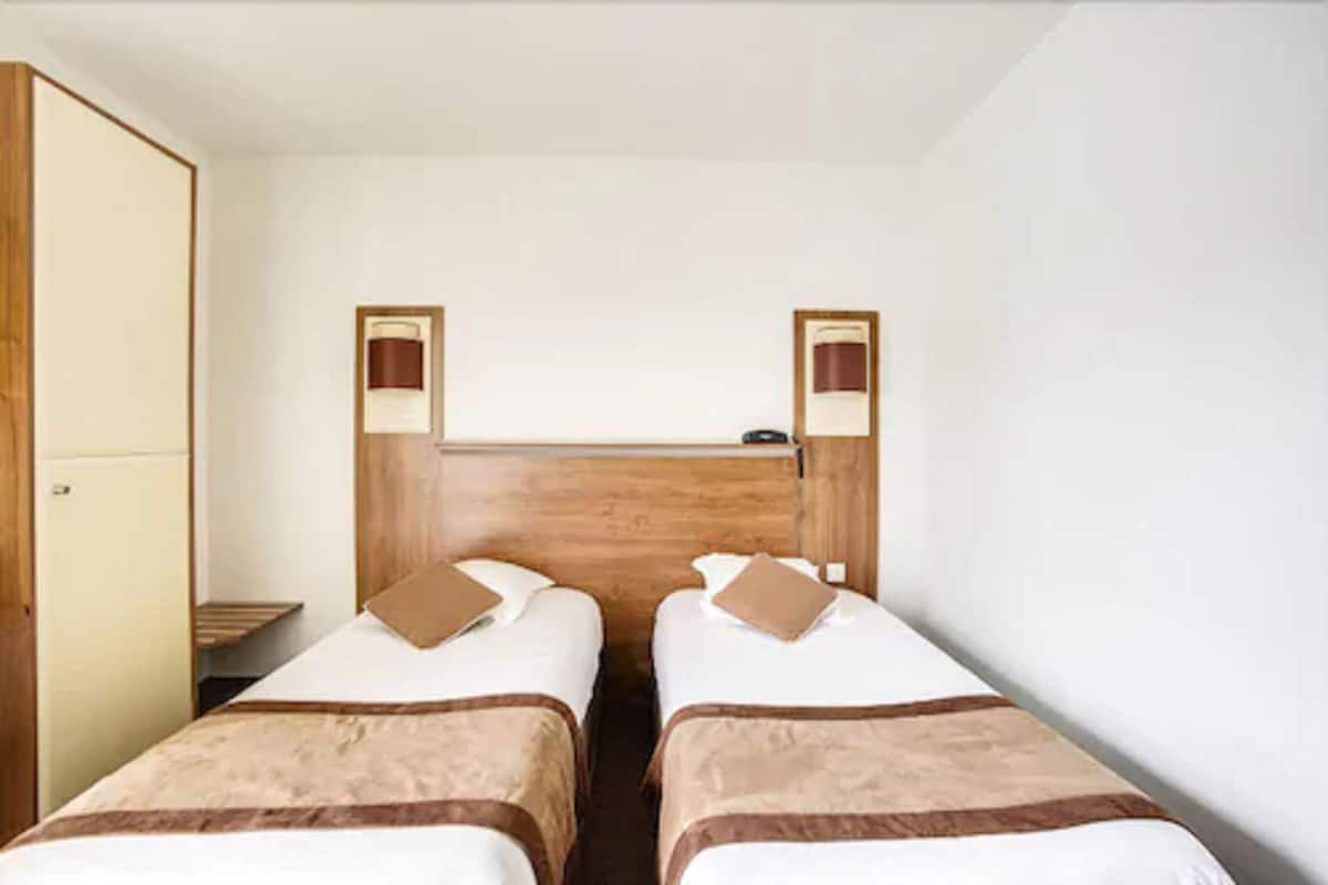 Une chambre avec deux lits simples, une armoire en bois et une petite étagère au-dessus des lits.