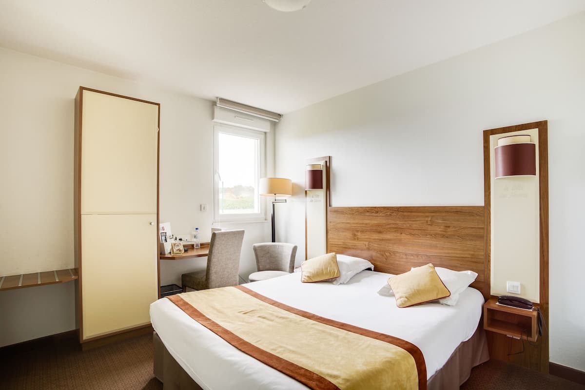 Une chambre d’hôtel avec un grand lit, un bureau, une chaise, une armoire et une fenêtre.