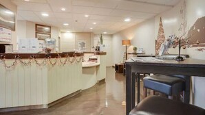 A reception area with a counter, seating, and a decorative tree on the wall. - Brit Hotel La Cote Des Havres (Lessay)