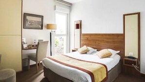A hotel room with a bed, a desk, a chair, a lamp, and a window. - Brit Hotel La Cote Des Havres (Lessay)