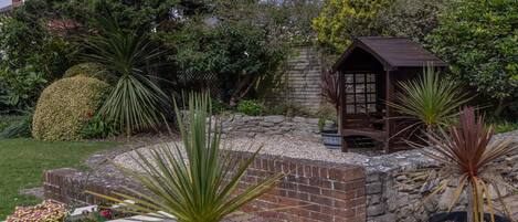 A garden with a wooden gazebo, a brick wall, and various plants.