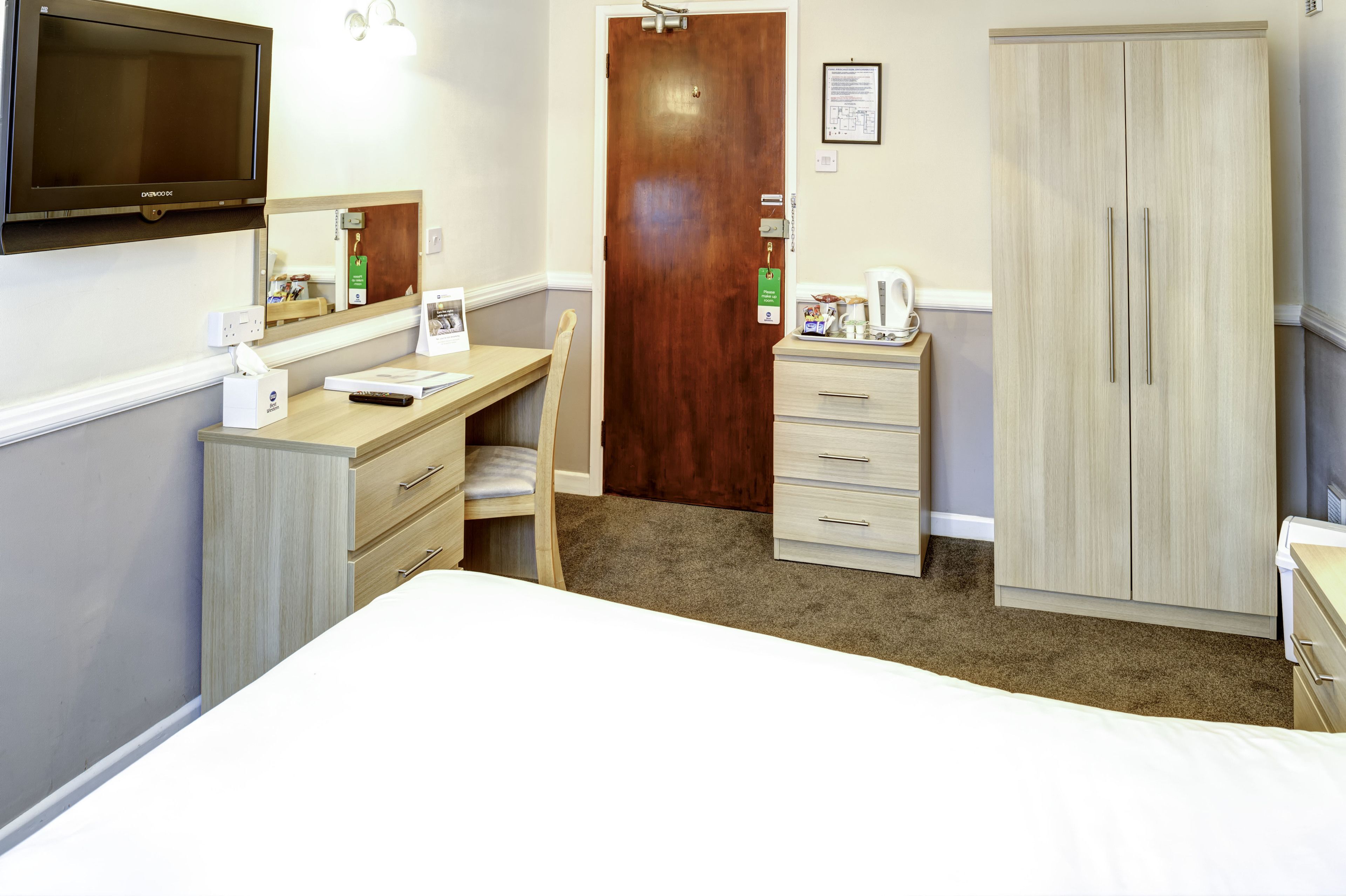 Habitación de hotel con cama, escritorio, silla, armario, televisor y espejo.