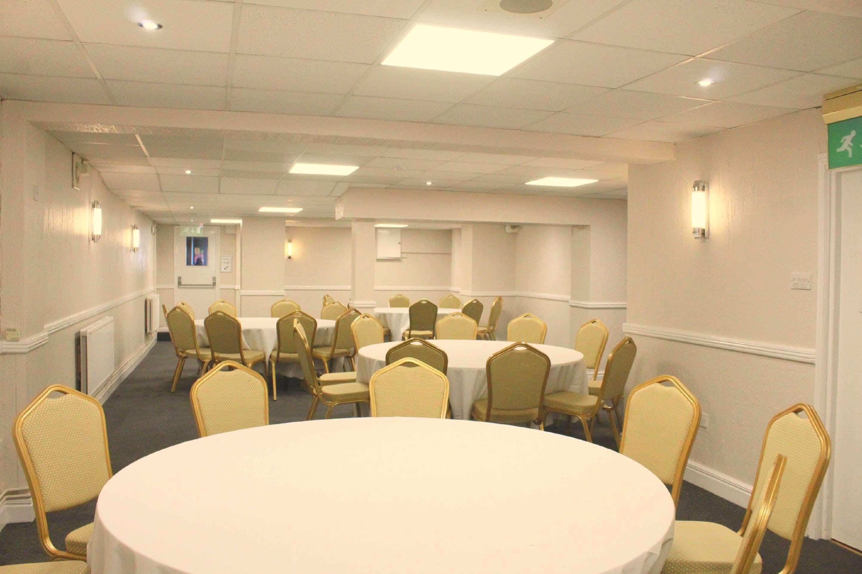 A conference room with multiple round tables and chairs, equipped with ceiling lights and wall-mounted lamps.