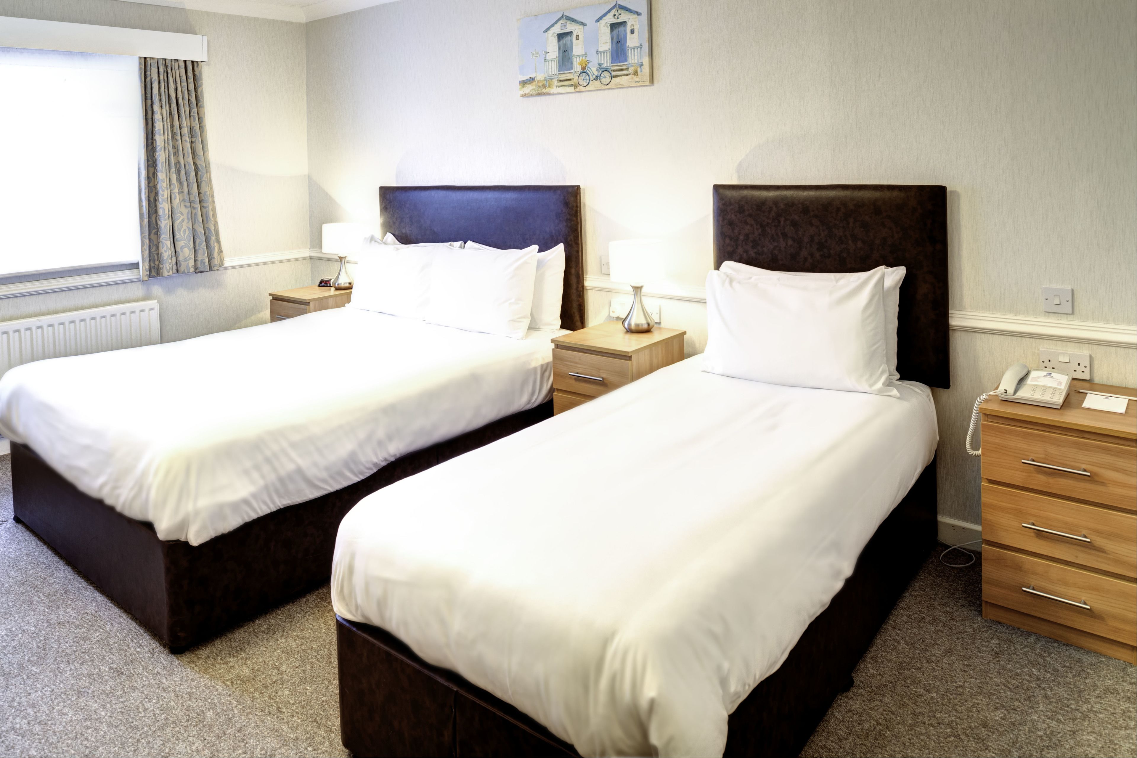 Two single beds with wooden headboards, bedside tables with lamps, and a painting on the wall.
