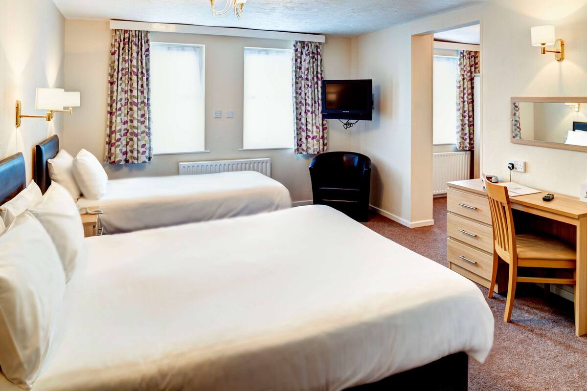 A hotel room with two beds, a desk, a chair, a television, and a window with curtains.