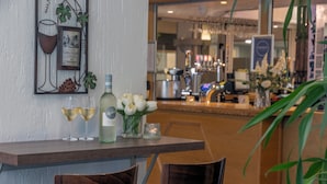 A bar area with a wooden counter, two chairs, a wine glass, a bottle, and a vase with flowers. - Best Western Weymouth Hotel Rembrandt (Weymouth)