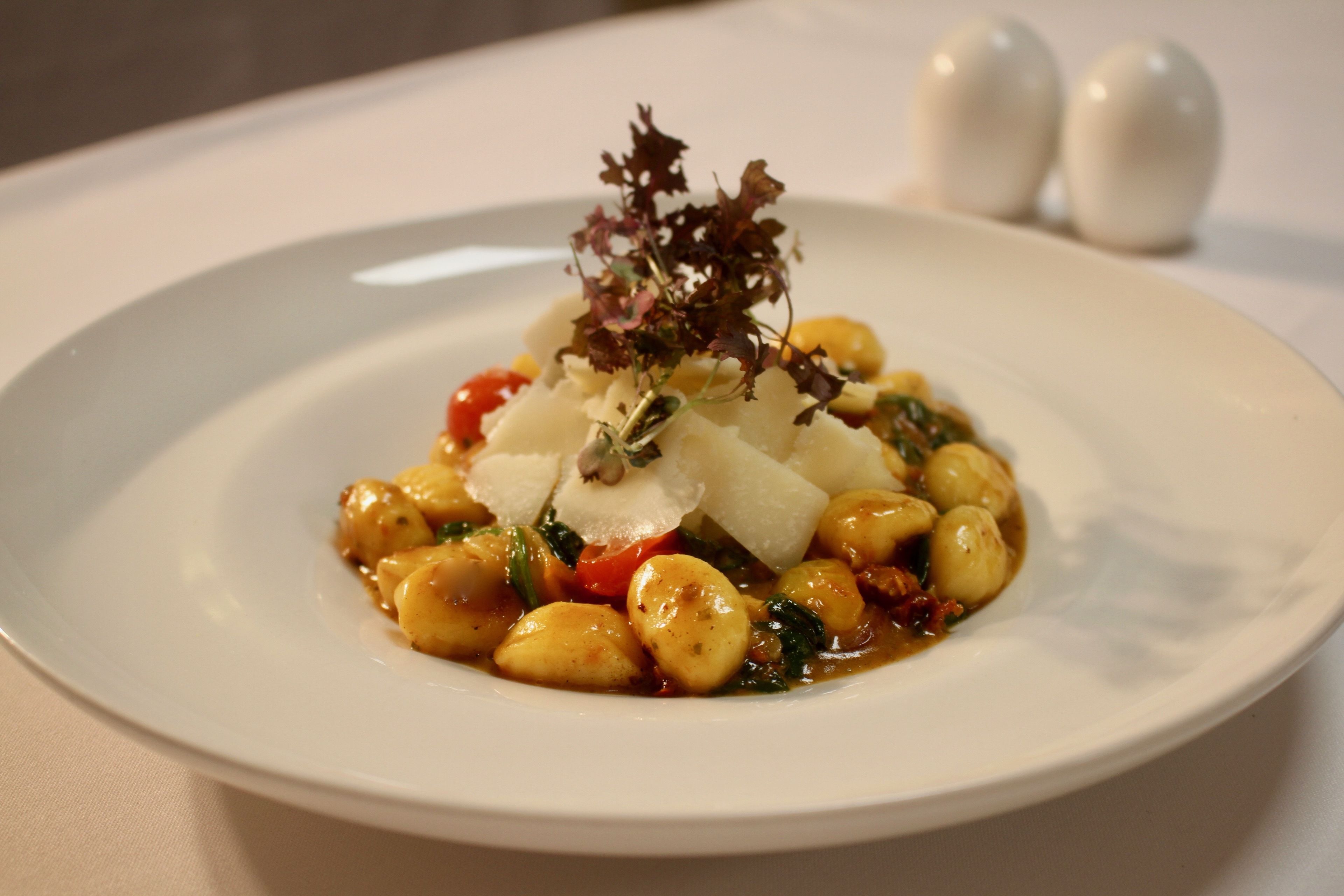 En tallrik med mat bestående av gnocchi, tomater och en garnering, serverat på en vit tallrik.