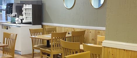 Ein Restaurantinneres mit Holztischen und -stühlen, einer Theke mit einer Kaffeemaschine und zwei runden Spiegeln an der Wand.