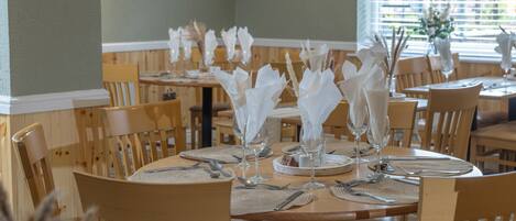 Un restaurante con mesas y sillas de madera, adornado con servilletas blancas, cubiertos y copas.