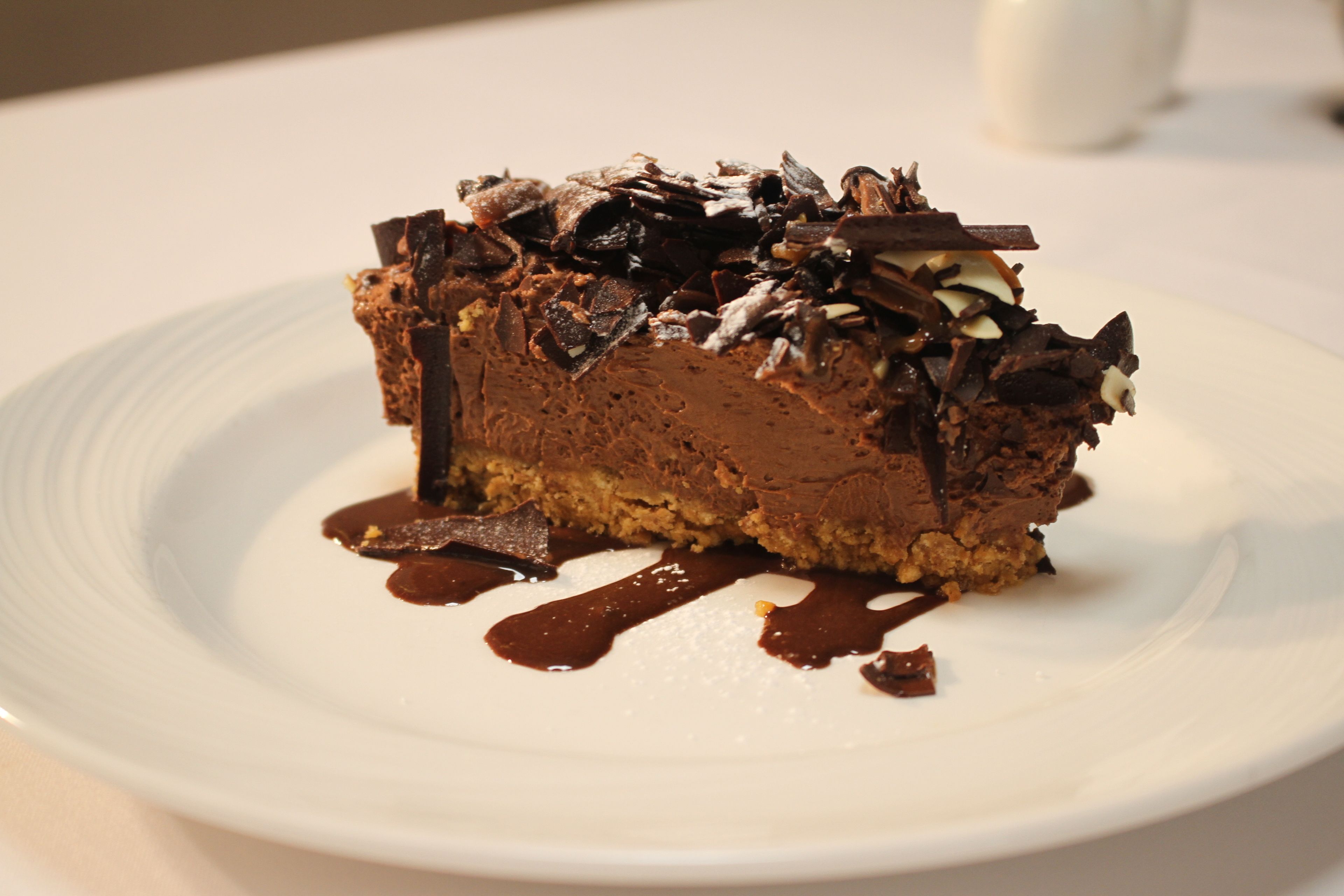 A slice of chocolate cake with chocolate shavings and a drizzle of chocolate sauce on a white plate.