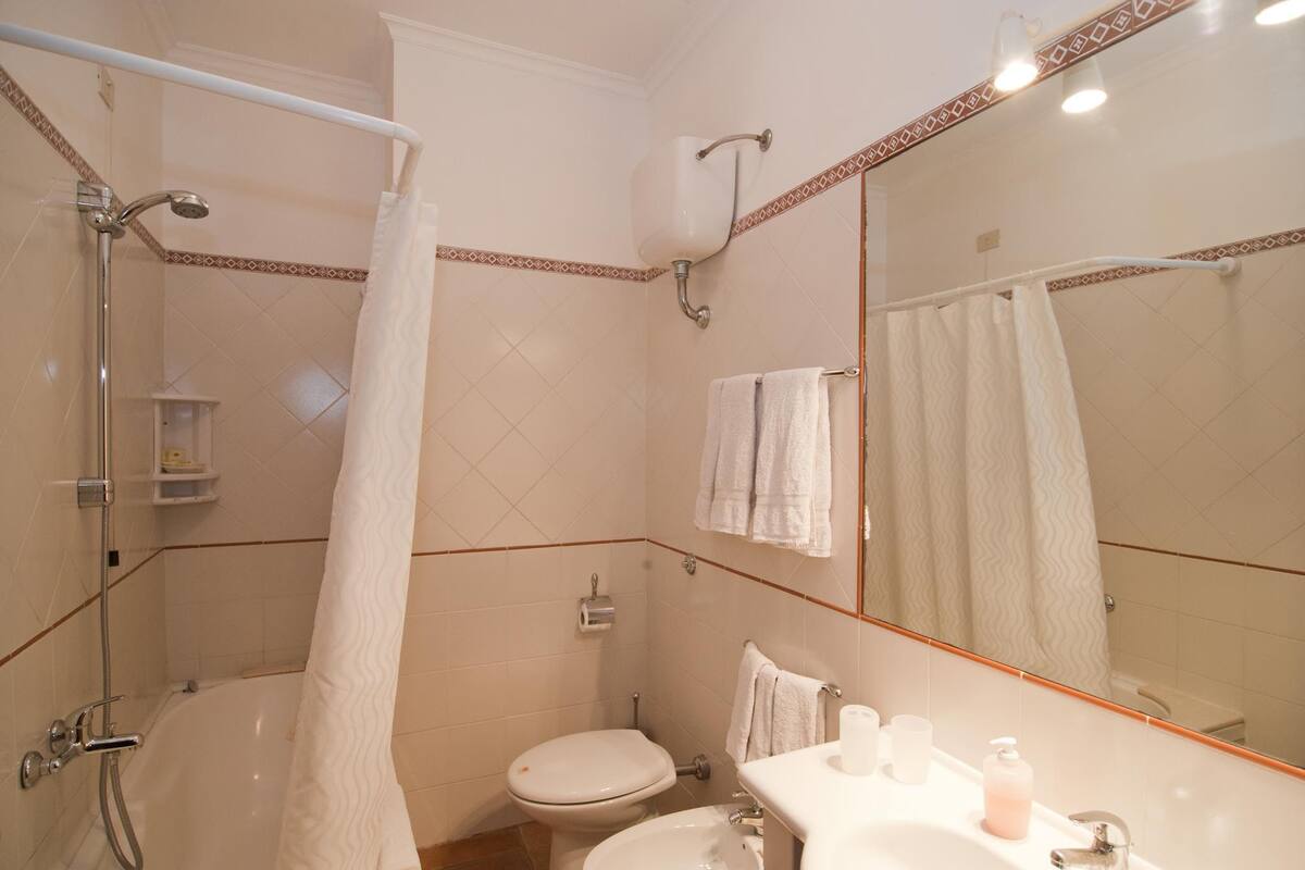 Een badkamer met een douche, toilet, wastafel en een grote spiegel.