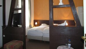 A hotel room with a bed, a nightstand, a lamp, a television, and a window with curtains. - TM Apart Hotel Essen (Essen)