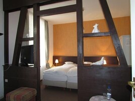 Una habitación de hotel con cama, mesita de noche, lámpara, televisor y ventana con cortinas.