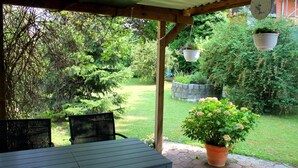A covered patio with a table and chairs, surrounded by lush greenery and a stone wall. - TM Apart Hotel Essen (Essen)