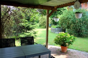 Un patio cubierto con una mesa y sillas, rodeado de abundante follaje y un muro de piedra.
