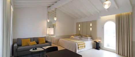 A modern hotel room with a sofa, a bed, a table, and a large window with curtains.