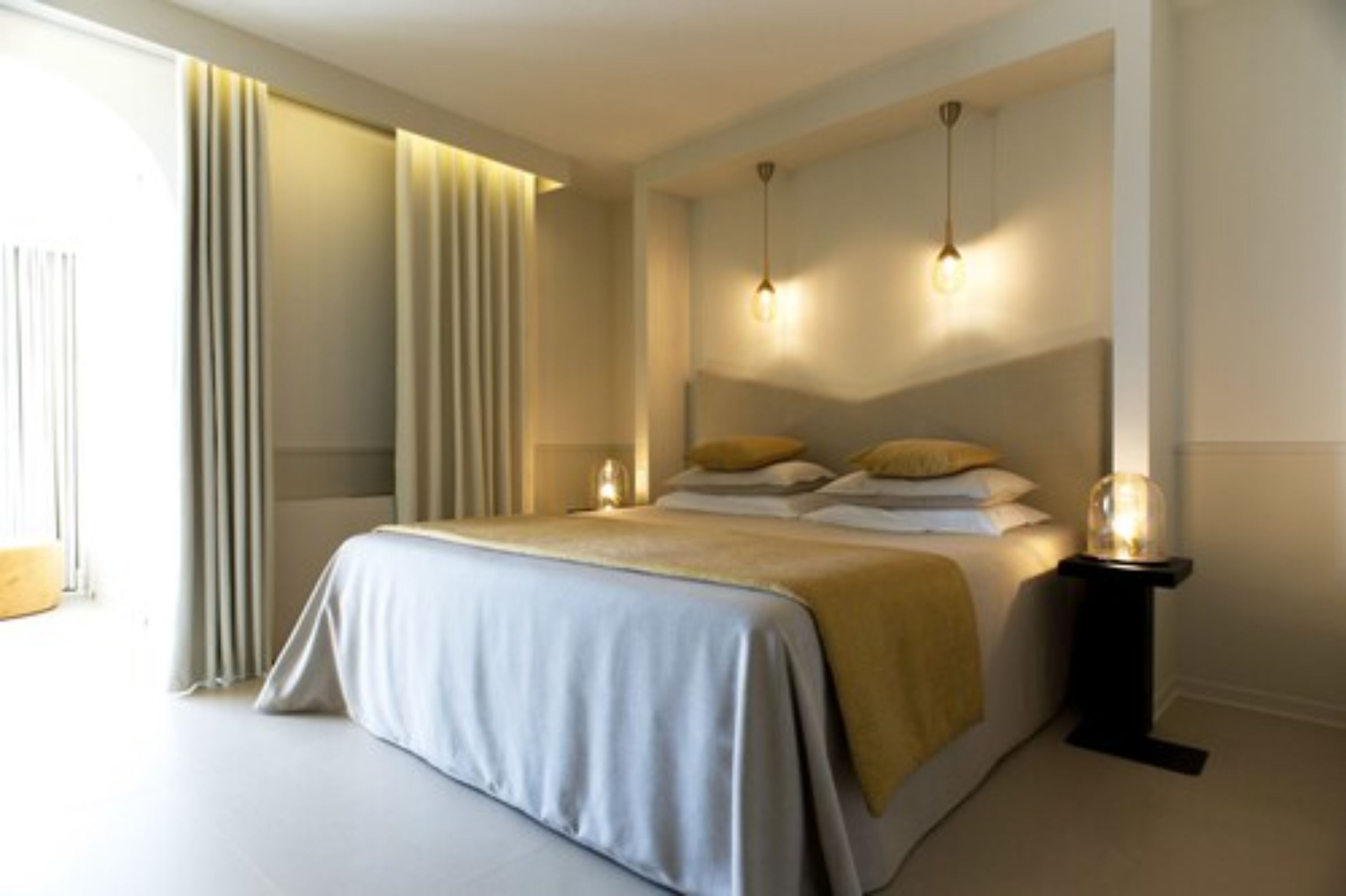 A modern bedroom with a large bed, bedside lamps, and a view of the outdoors.