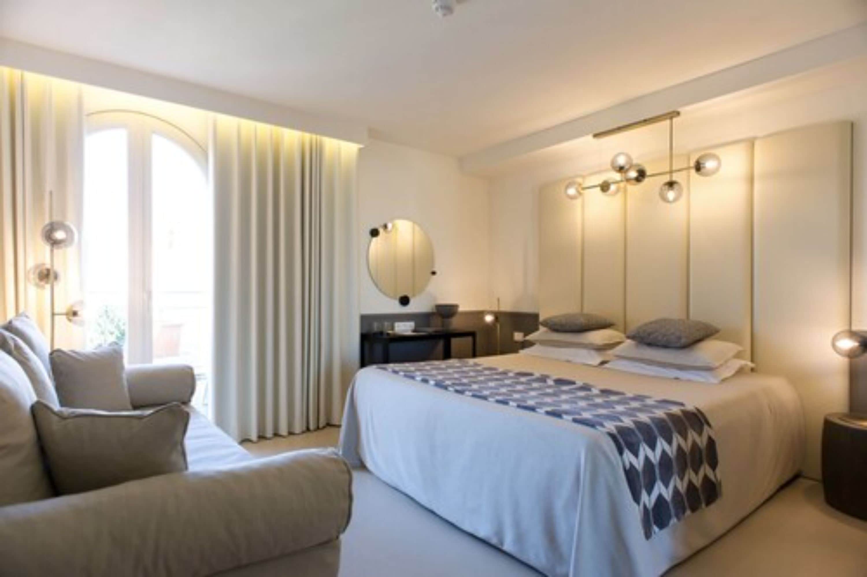 Une chambre d’hôtel moderne avec un grand lit, un canapé, un bureau et une grande fenêtre avec des rideaux.