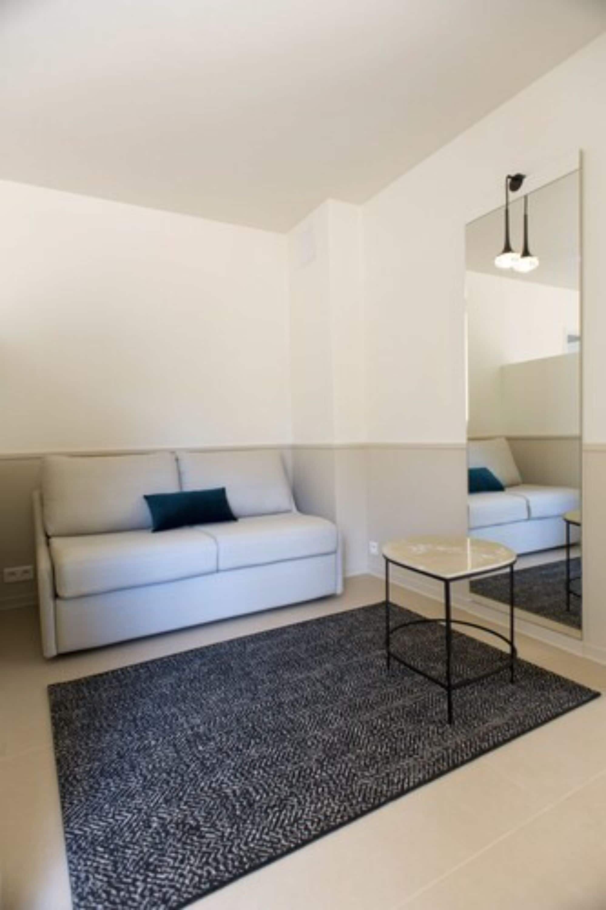 A minimalist living room with a white sofa, a small round table, and a large mirror on the wall.