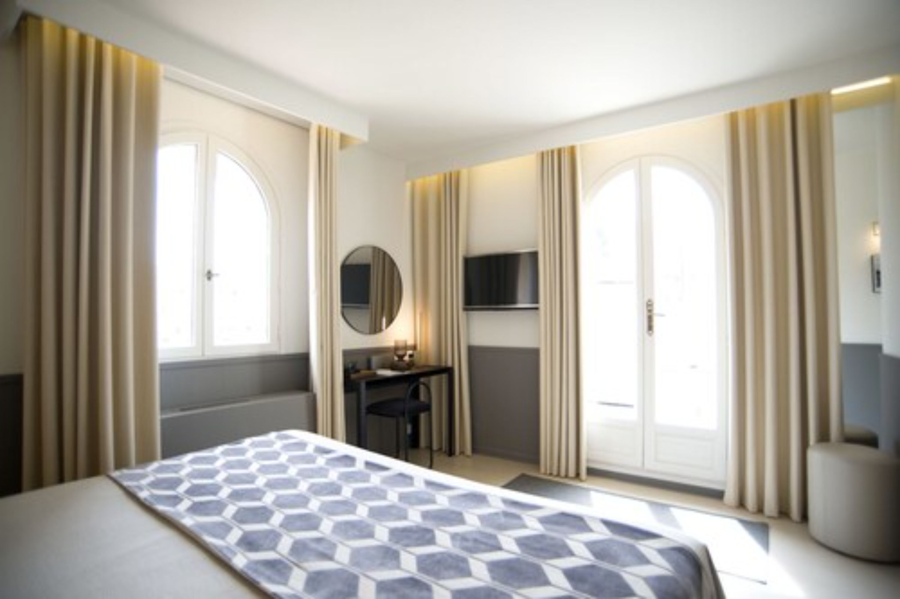 Une chambre d’hôtel avec un lit, un bureau, une télévision et une grande fenêtre avec des rideaux.