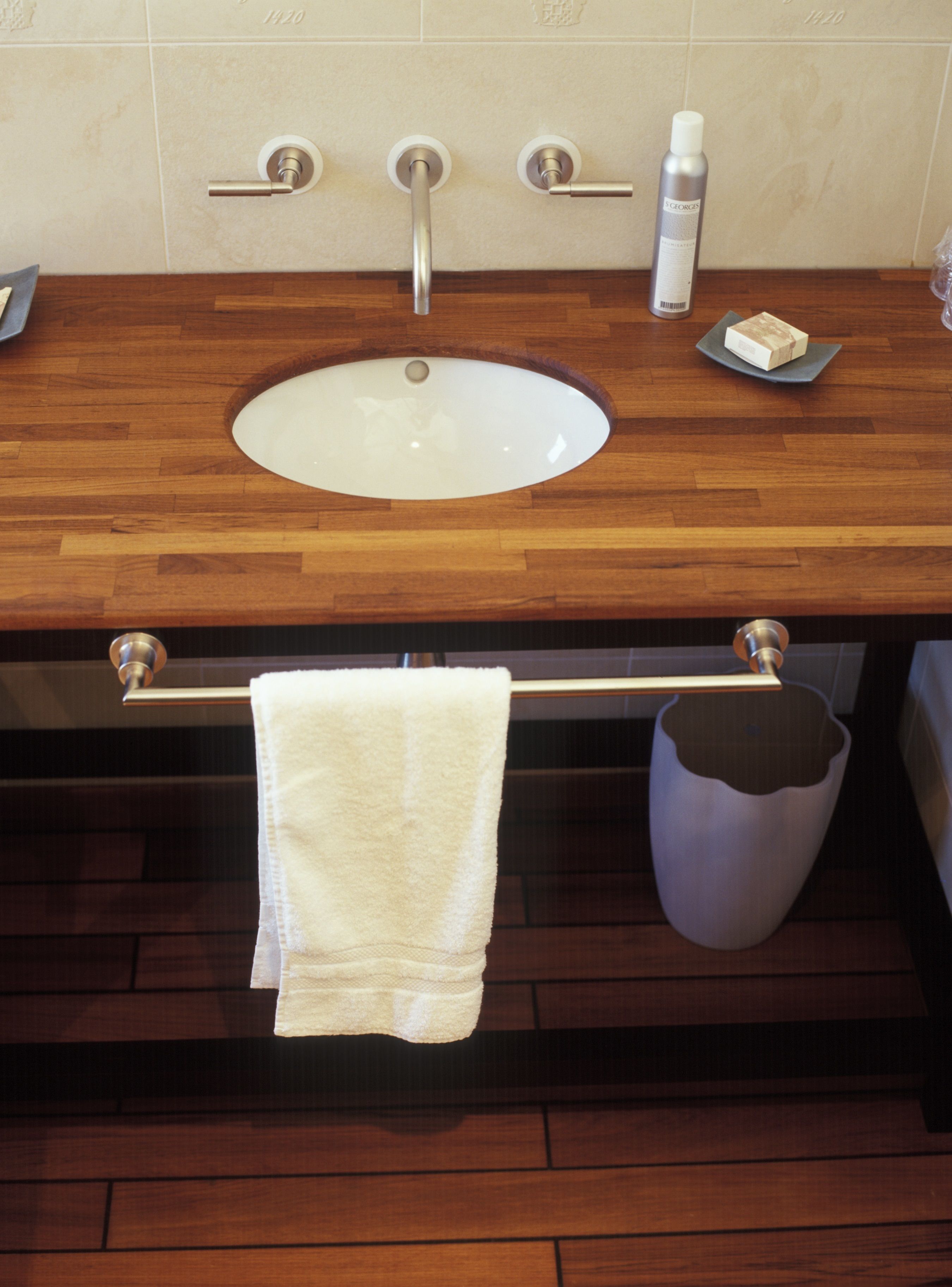 A bathroom with a wooden vanity, a white sink, a towel rack, and a trash can.
