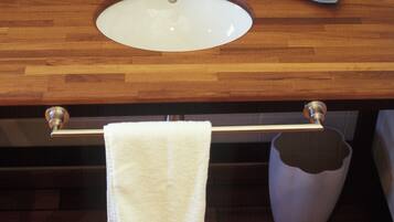 A bathroom with a wooden vanity, a white sink, a towel rack, and a trash can.