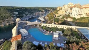 A coastal hotel with a large swimming pool, sun loungers, and a view of the marina and historic buildings. - Hotel Genovese (Bonifacio)