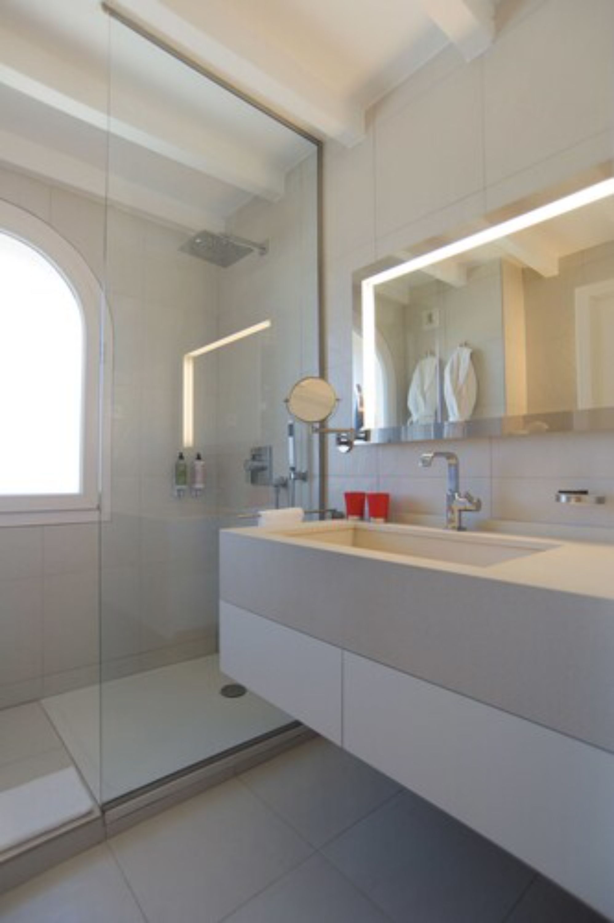 A modern bathroom with a glass shower enclosure, a large mirror, and a white vanity with a sink.