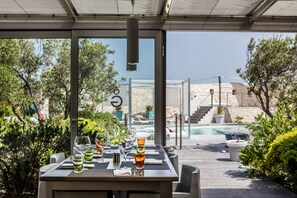 An outdoor dining area with a pool view, tables set with glasses and napkins, and a modern architectural design. - Hotel Genovese (Bonifacio)