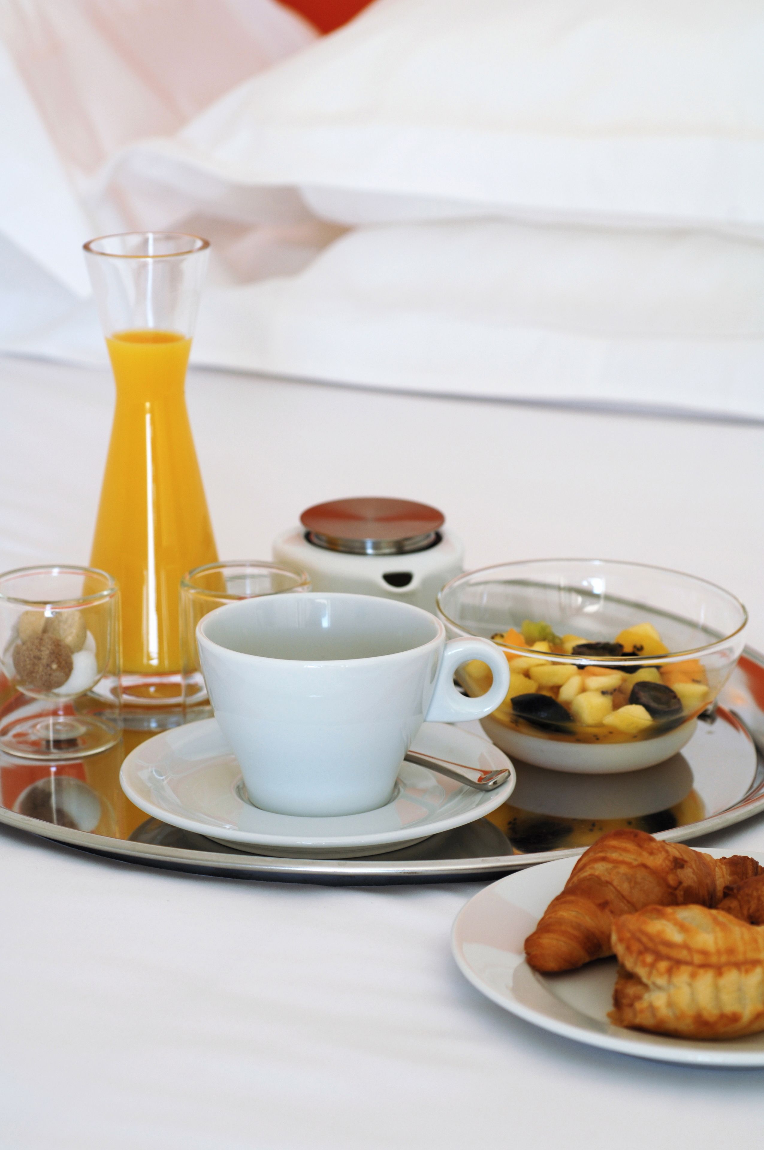 Una bandeja de desayuno con un vaso de jugo de naranja, una taza, un bol de fruta y croissants.