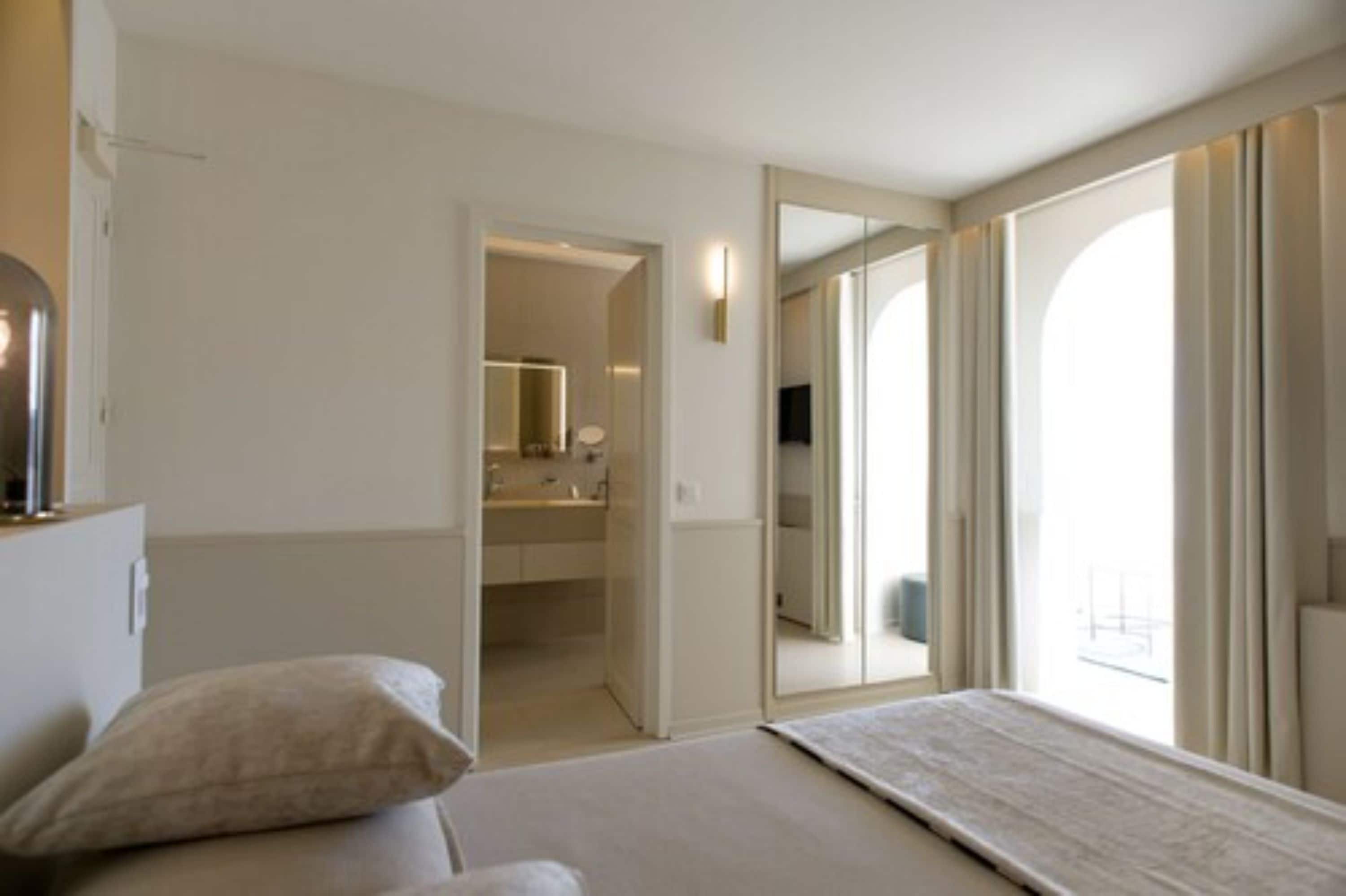 Un dormitorio con cama, mesita de noche, espejo y vistas al baño.