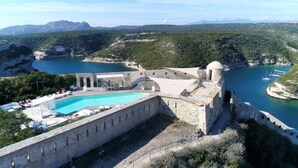 A coastal hotel with a swimming pool, a view of the sea, and a mountainous backdrop. - Hotel Genovese (Bonifacio)
