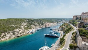 A coastal marina with yachts docked, a road alongside, and a historic building on a cliff. - Hotel Genovese (Bonifacio)