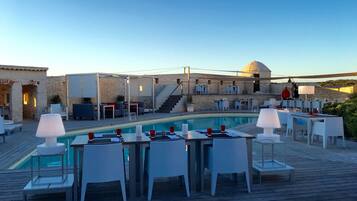 A poolside area with tables and chairs, a stone wall, and a staircase leading to an upper level.