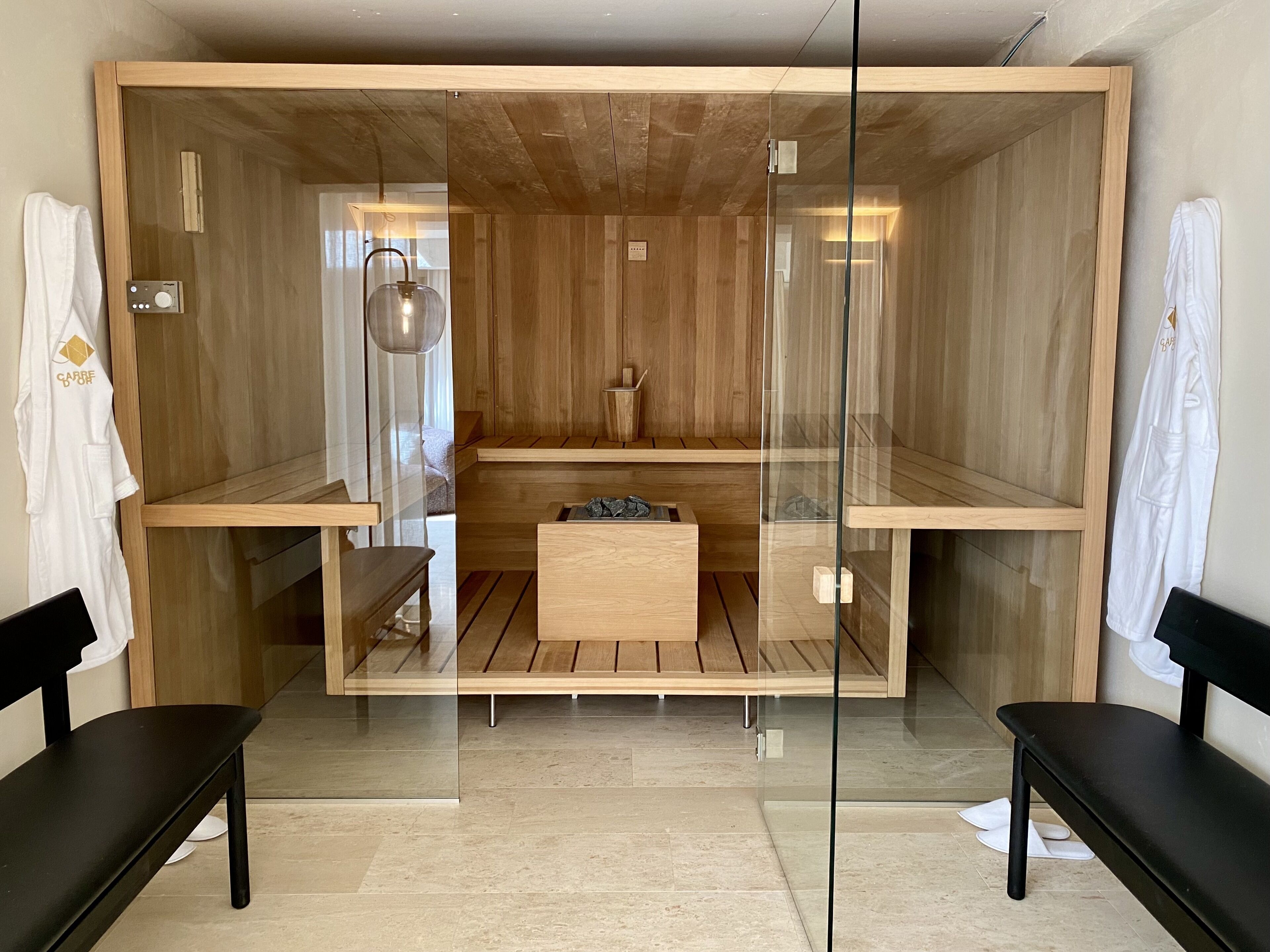 Uma sauna moderna com paredes e bancos de madeira, um painel de controle e uma pequena mesa no centro.