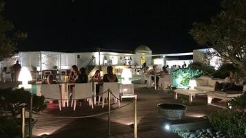 Ein Außenbereich zum Essen mit Tischen und Stühlen, umgeben von Grünpflanzen und einem Pool.