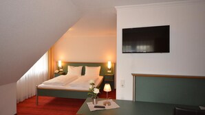 A hotel room with a bed, bedside tables, a TV mounted on the wall, and a small desk with a lamp.