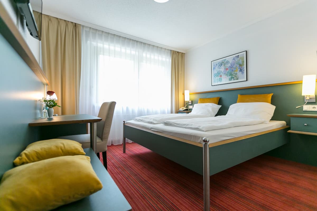 Een hotelkamer met een bed, een bureau, een stoel en een tafeltje met een bloevas.