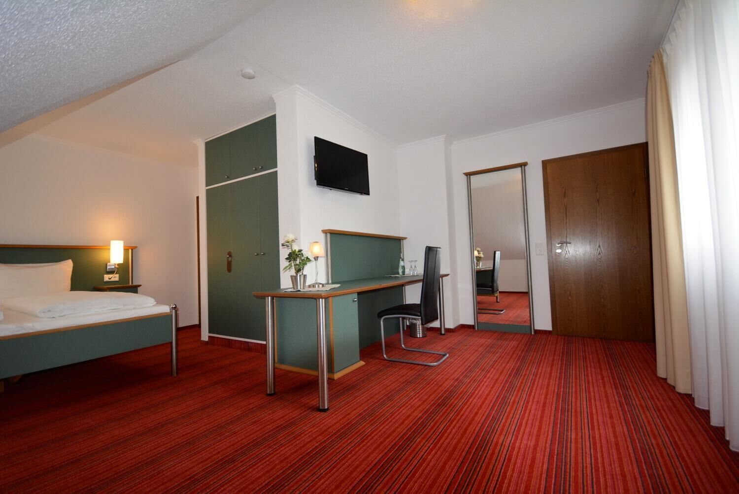 Una habitación de hotel con cama, escritorio, silla y espejo.