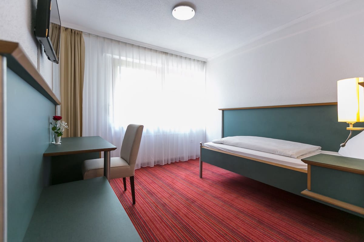 Een hotelkamer met een bed, bureau, stoel, televisie en raam met gordijnen.