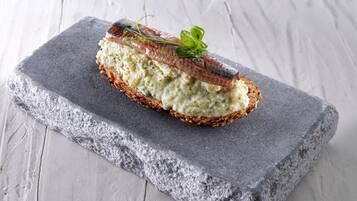 A slice of bread with a creamy spread and a piece of fish on top, placed on a gray stone slab.