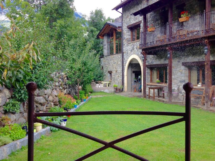 A stone building with a stone facade, a wooden balcony, and a small garden area with a lawn and a stone wall.