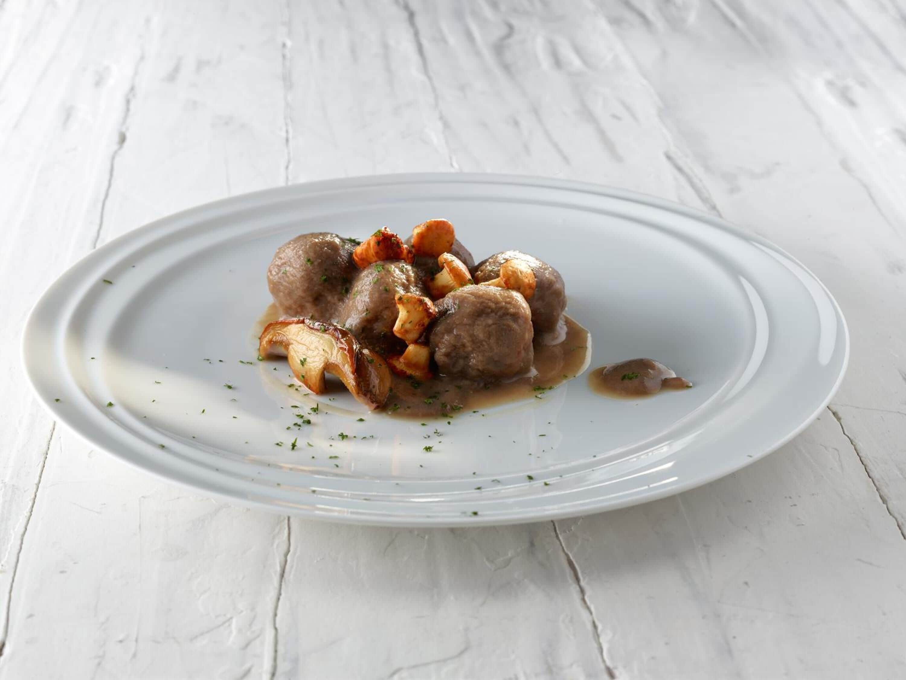 A white plate with meatballs and roasted potatoes on a white wooden table.