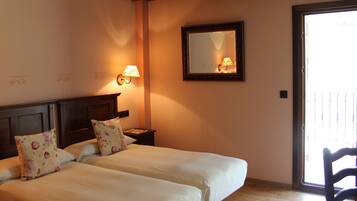Habitación de hotel con dos camas, una mesita de noche, un espejo en la pared y una puerta corrediza de cristal.