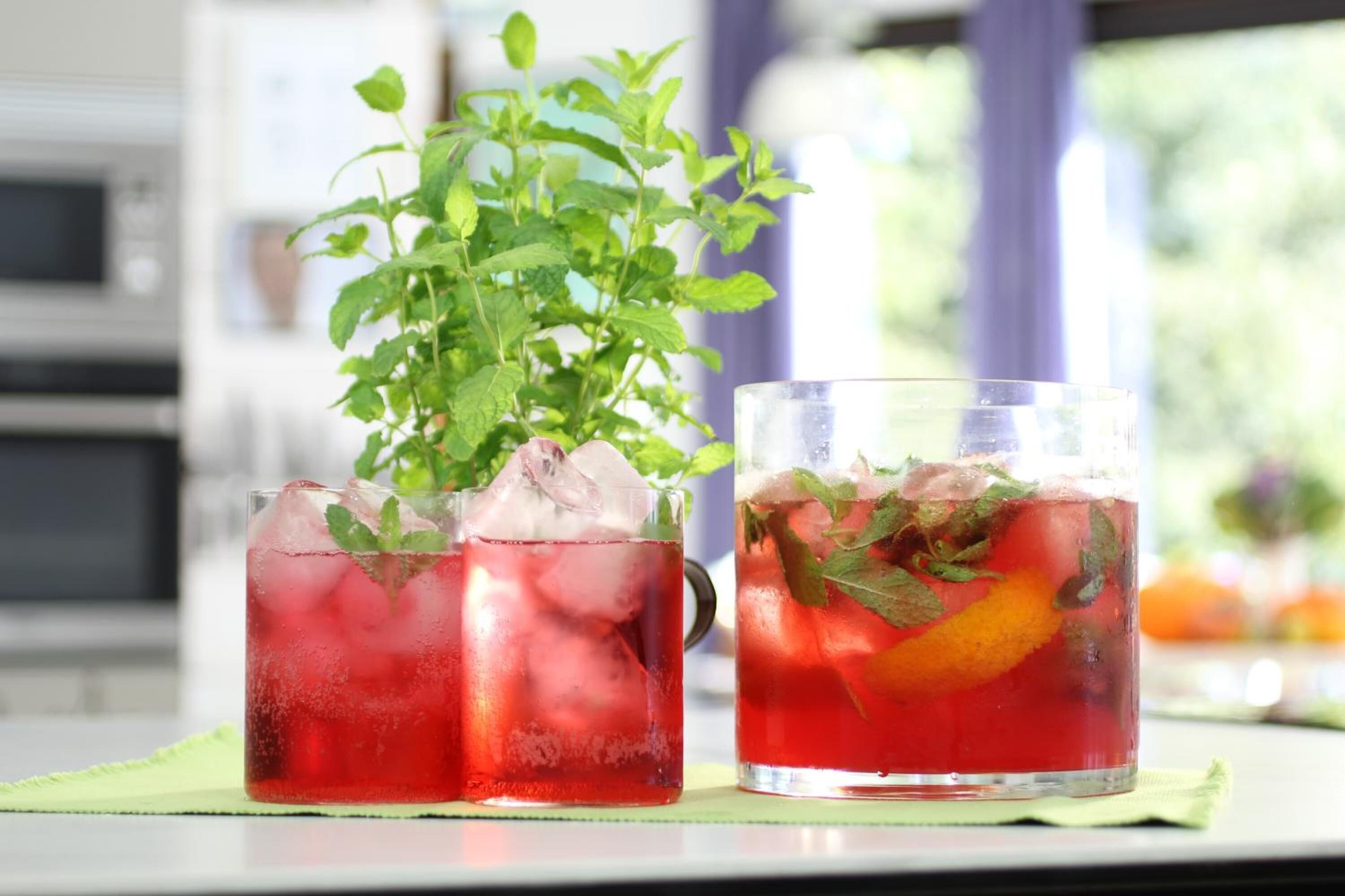 Dos vasos de bebida roja con hielo y hojas de menta, sobre un tapete verde.