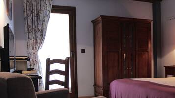 A bedroom with a bed, a wooden wardrobe, a desk with a chair, and a lamp.