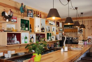 Zona de bar con estantes de madera, botellas, vasos y una planta.