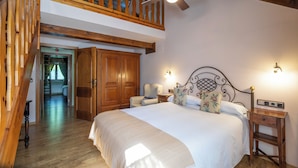 A bedroom with a large bed, wooden wardrobe, and a loft area with a wooden staircase. - Hotel Casa Arcas (Villanova)